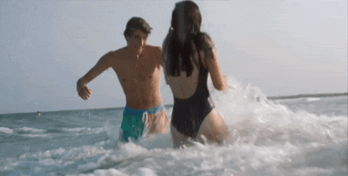 a man and a woman in swimsuits are playing in the ocean