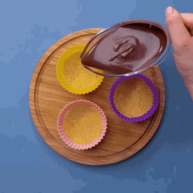 a person pouring chocolate into cupcake liners on a cutting board