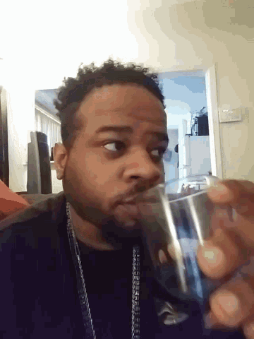 a man in a black shirt is drinking from a clear glass