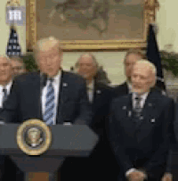 a man in a suit and tie is standing at a podium in front of a group of men .