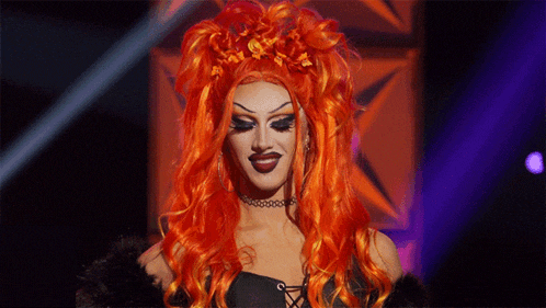 a drag queen with red hair and a choker looks at the camera