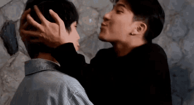 a man is kissing another man on the forehead while holding his head .