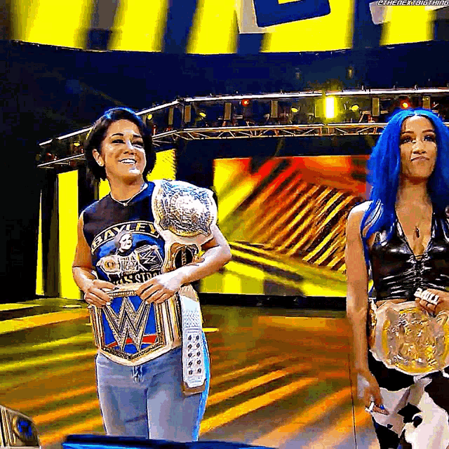 two women are standing on a stage holding a wrestling championship belt