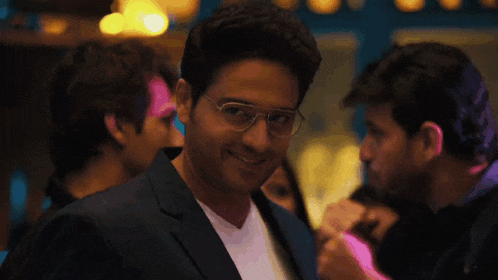 a man wearing glasses and a suit smiles in a crowd of people