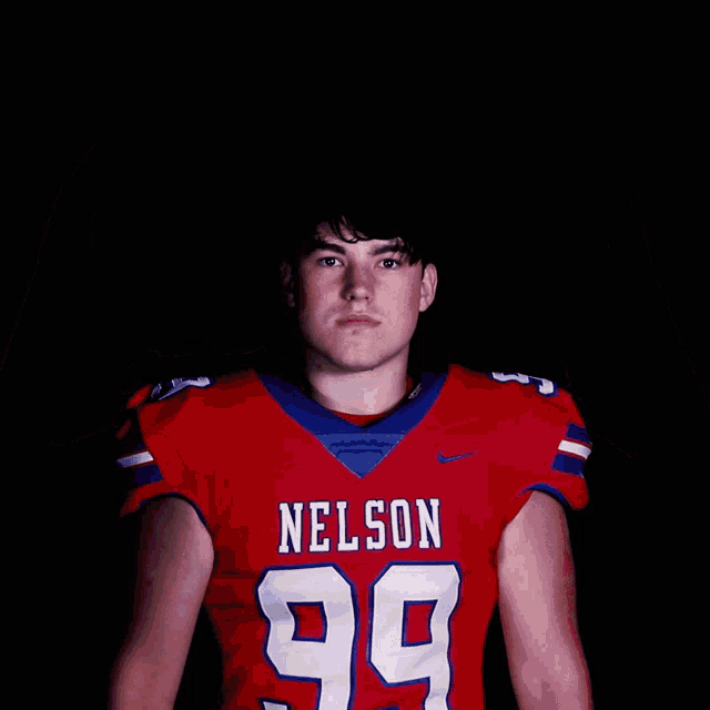 a young man wearing a nelson 99 jersey stands with his hands in the air