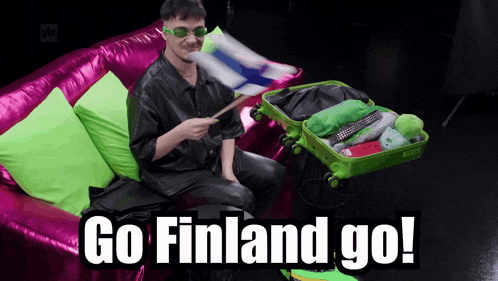 a man is sitting on a pink couch with a green suitcase that says " go finland go "