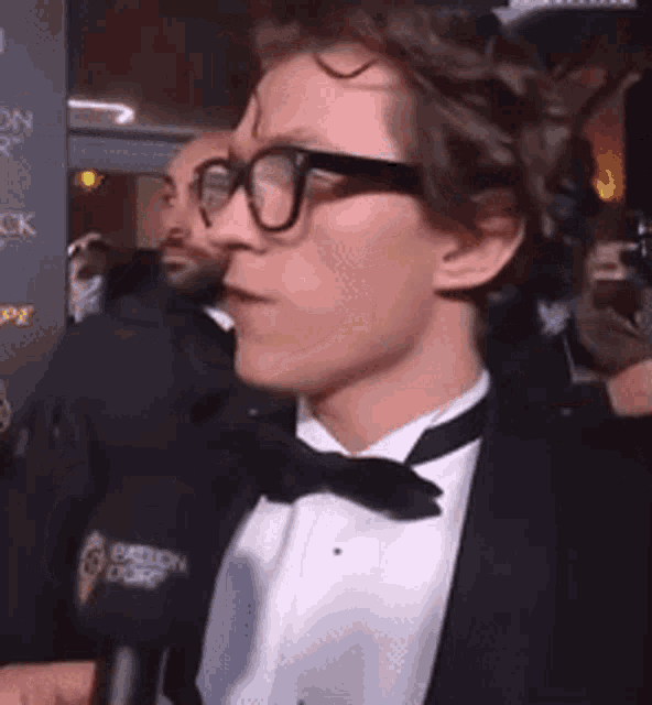 a man wearing glasses and a tuxedo is talking into a microphone in front of a wall that says passion corp
