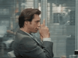 a man in a suit and tie is sitting in front of a window and making a funny face .