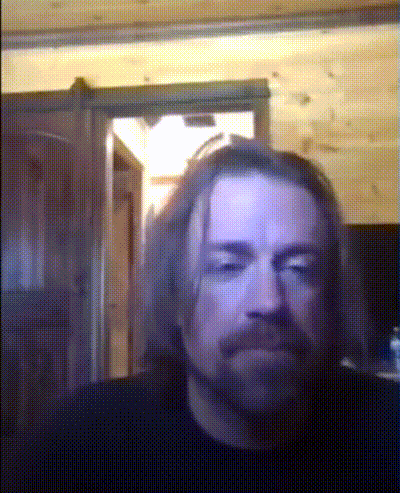 a man with long hair and a beard looks at the camera with a door in the background