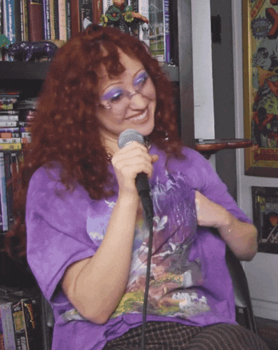 a woman in a purple shirt is singing into a microphone in front of a bookshelf with a book titled the farse
