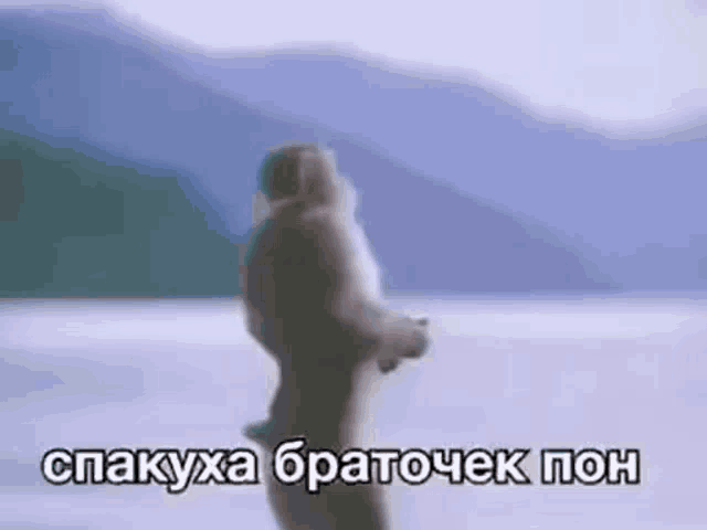 a naked man is standing in the snow with mountains in the background and a caption in a foreign language .