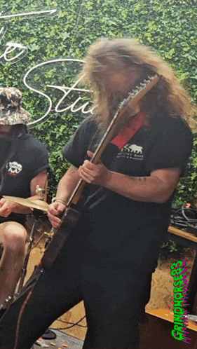 a man with long hair is playing a guitar in front of a sign that says stu
