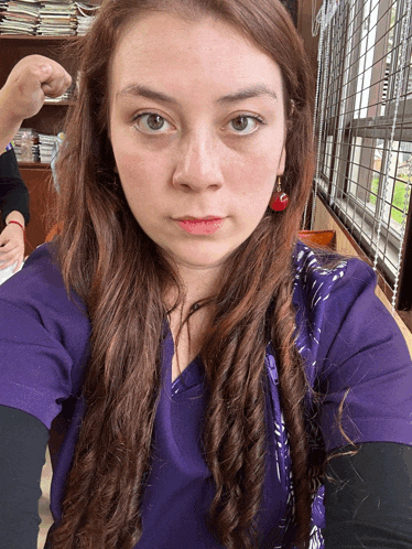 a woman in a purple scrub top takes a selfie in front of a window