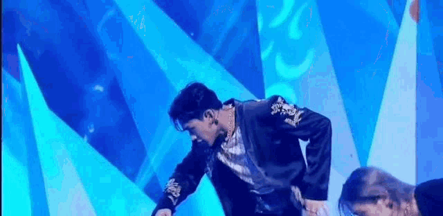 a man in a black jacket is dancing on a stage with a blue background .
