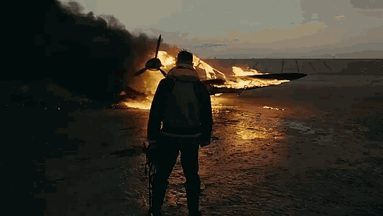 a man is standing in front of a burning plane on the beach