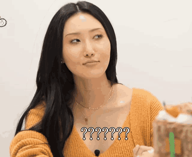 a woman wearing an orange sweater and a necklace has a question mark above her chest