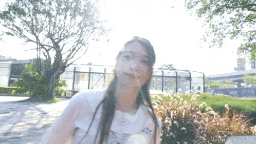 a woman in a white shirt is standing in front of a fence and a sign that says gifbin.com