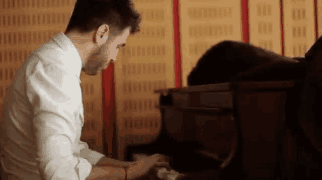 a man in a white shirt is playing a piano in a room
