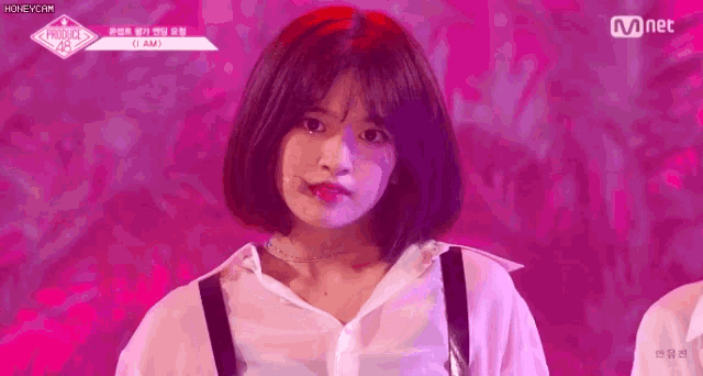 a girl with short hair and a white shirt is standing on a stage with a pink background .