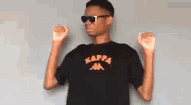 a young man wearing sunglasses and a kappa t-shirt is standing with his arms in the air .