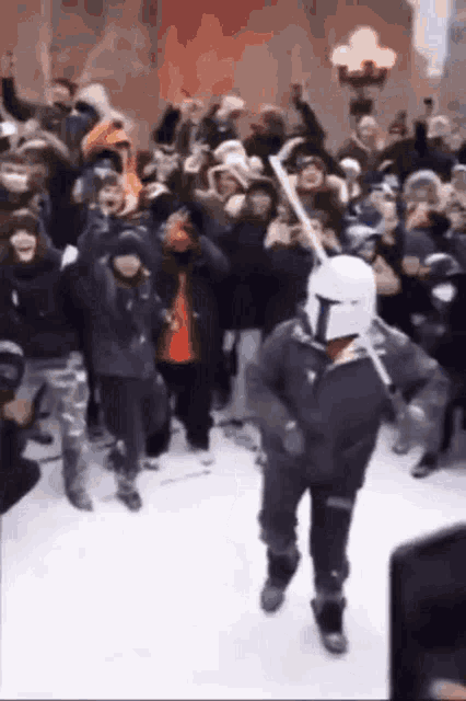 a man in a mandalorian helmet is holding a bat in front of a crowd of people .