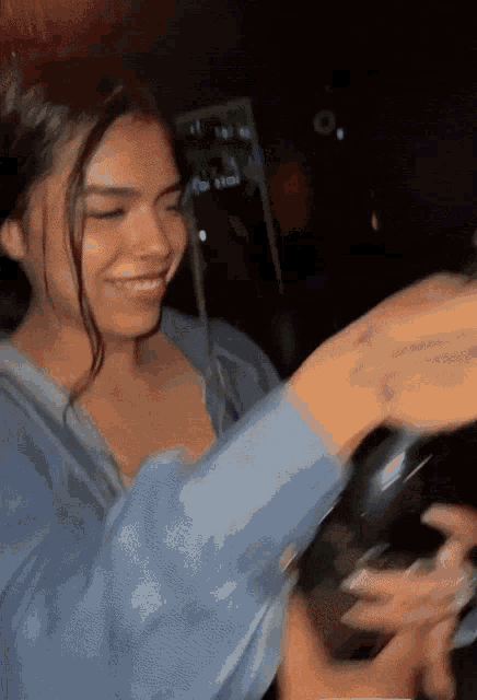 a woman in a blue shirt is smiling and holding a bottle of wine