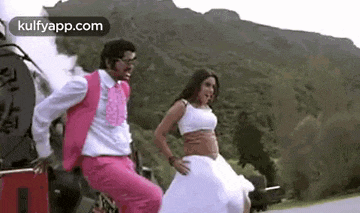 a man in a pink suit is riding on the back of a train next to a woman in a white dress .