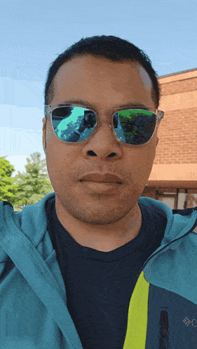 a man wearing a columbia jacket and sunglasses looks at the camera
