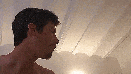 a man without a shirt is standing in front of a white wall and ceiling .