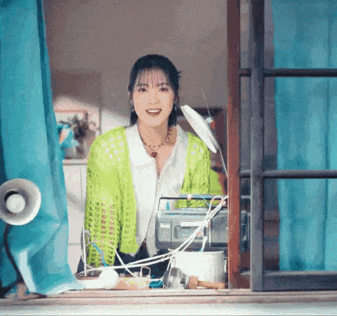 a woman in a green cardigan is sitting in front of a window with a radio on it .