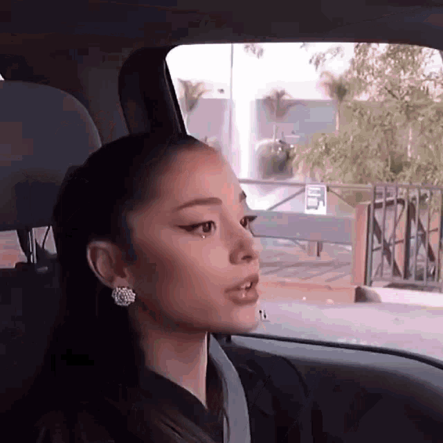 ariana grande is sitting in the back seat of a car with her eyes closed .