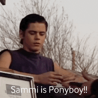 a young man in a purple tank top is holding a framed picture and says sammi is ponyboy .