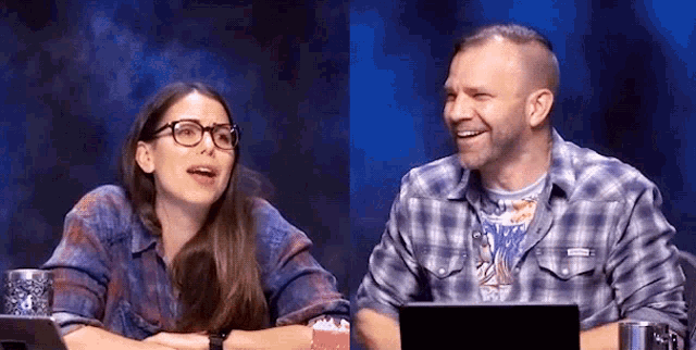a man and a woman are sitting next to each other at a table with a laptop and popcorn .