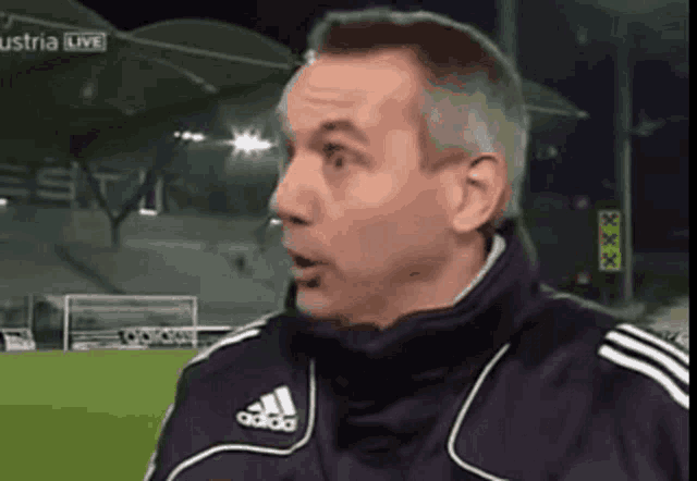 a man wearing an adidas jacket is standing on a soccer field