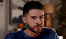 a man with a beard is wearing a blue sweater and making a funny face .