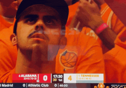 a man in an orange shirt watches a basketball game
