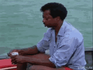 a man in a blue shirt is sitting on a boat looking at the water .
