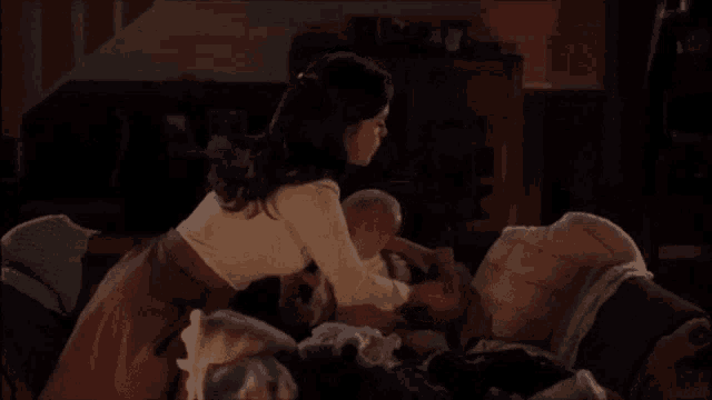a woman is holding a baby while sitting on a bed