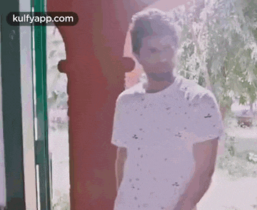 a man in a white t-shirt is standing in front of a window .