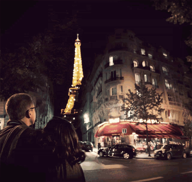 a man and a woman looking up at the eiffel tower at night