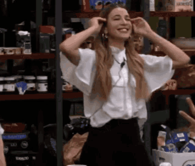 a woman in a white shirt and black skirt is standing in front of a shelf with her hands on her ears .