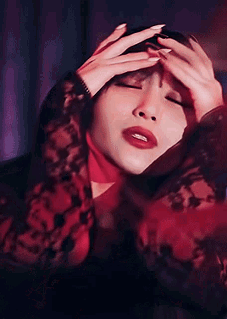 a woman in a red lace top is holding her head with her hands .
