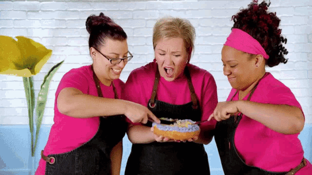 three women wearing pink aprons are looking at a cake