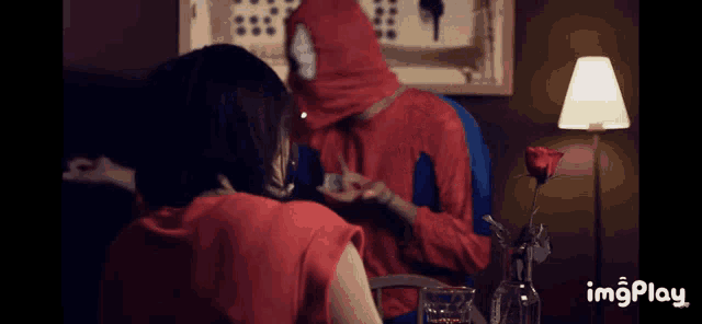 a man in a spiderman costume sits at a table with a woman in a red dress