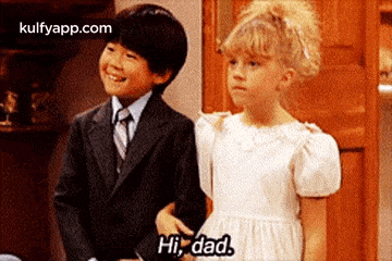 a boy in a suit and tie and a girl in a white dress are standing next to each other and talking .