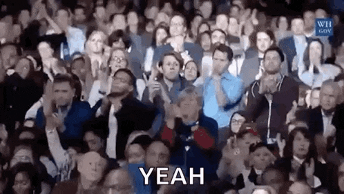 a large group of people are sitting in a stadium applauding and clapping .