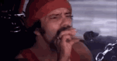 a man with a beard is smoking a cigarette while wearing a red hat .