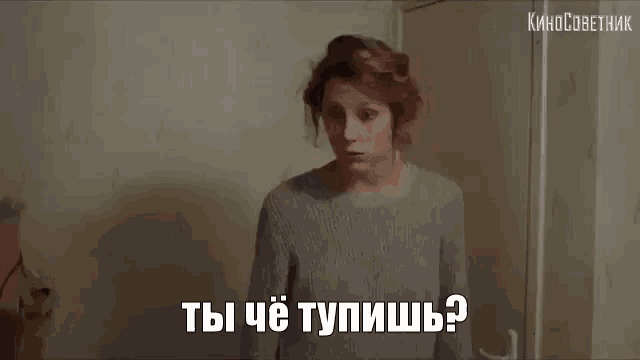 a woman in a grey sweater is standing in front of a door and talking in a foreign language .