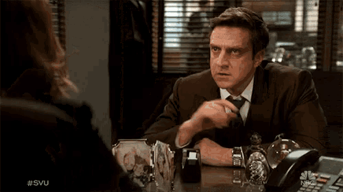 a man in a suit and tie is sitting at a desk with a phone and a picture of a family on it