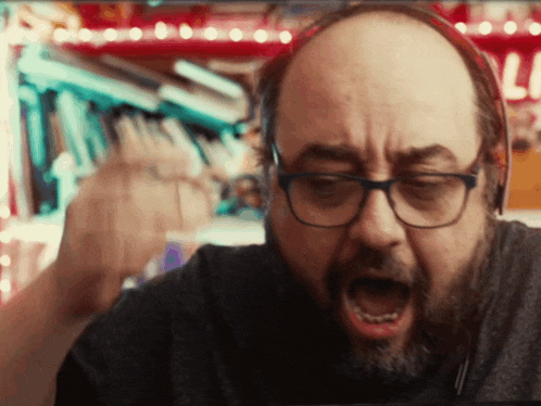 a bald man with glasses and a beard is wearing headphones and screaming